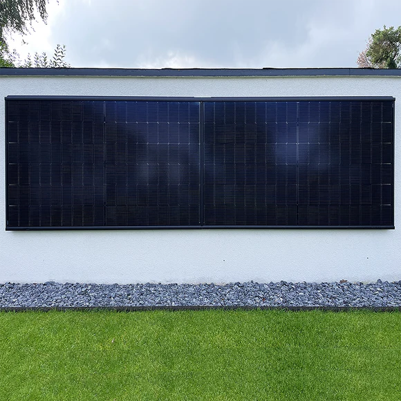 iSolarPro Installation von Solarmodulen an einer weißen Wand mit Kieselstein-Einfassung und Rasenfläche im Außenbereich